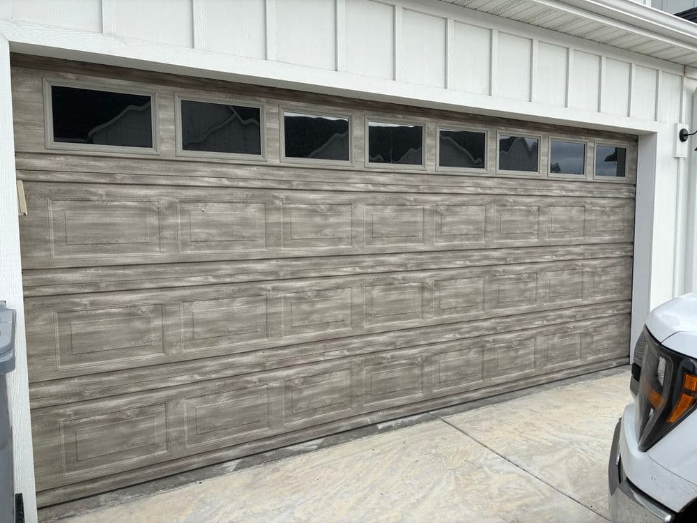Modern wooden garage door with windows, parked car in driveway, suburban home setting.