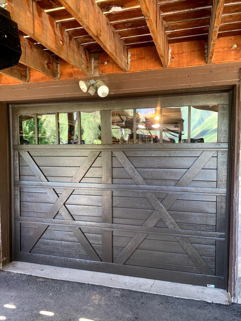 Modern wooden garage door with a rustic design, featuring diagonal patterns and windows.