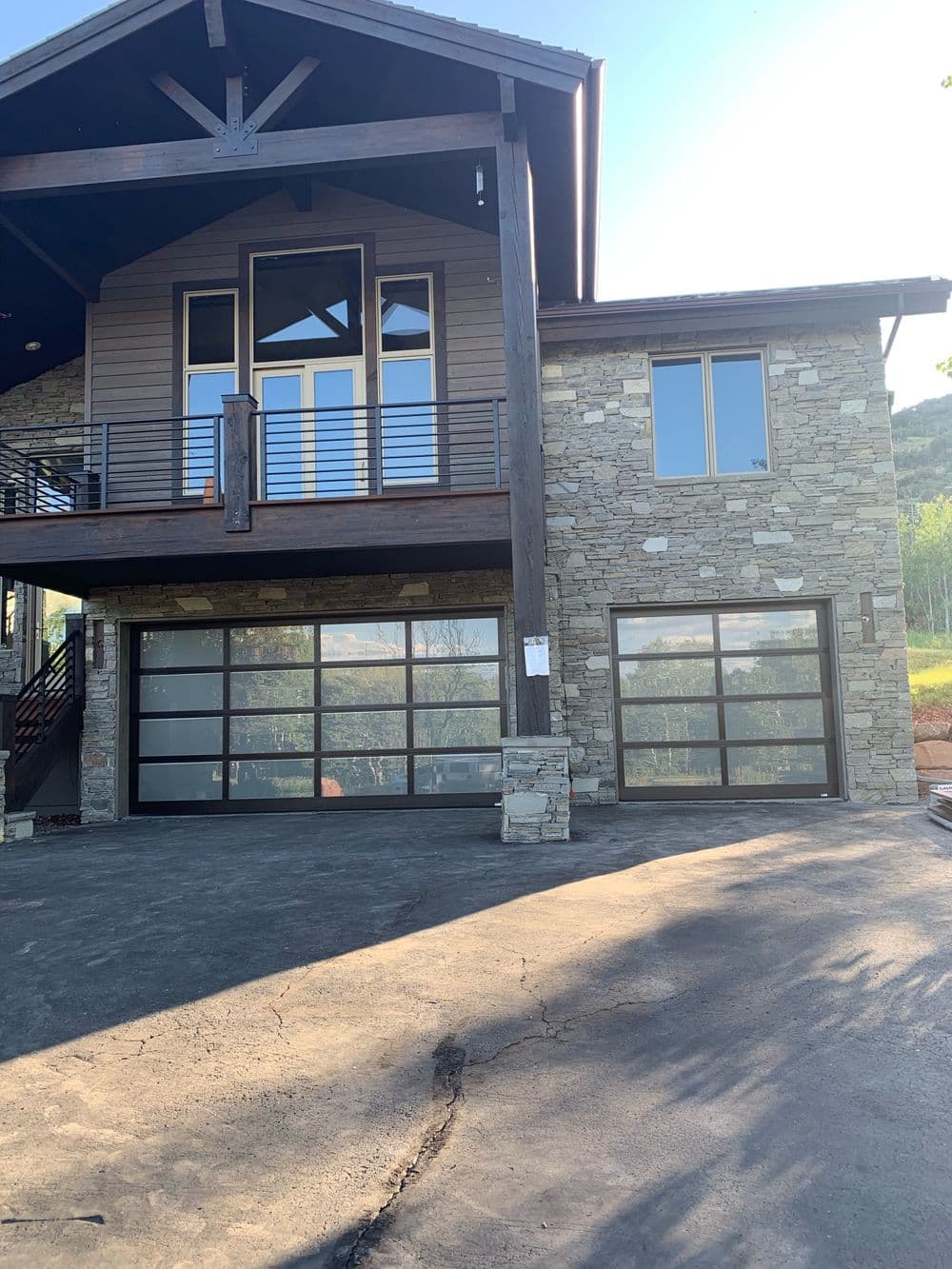 Modern stone house with large windows and glass garage doors in a scenic outdoor setting.