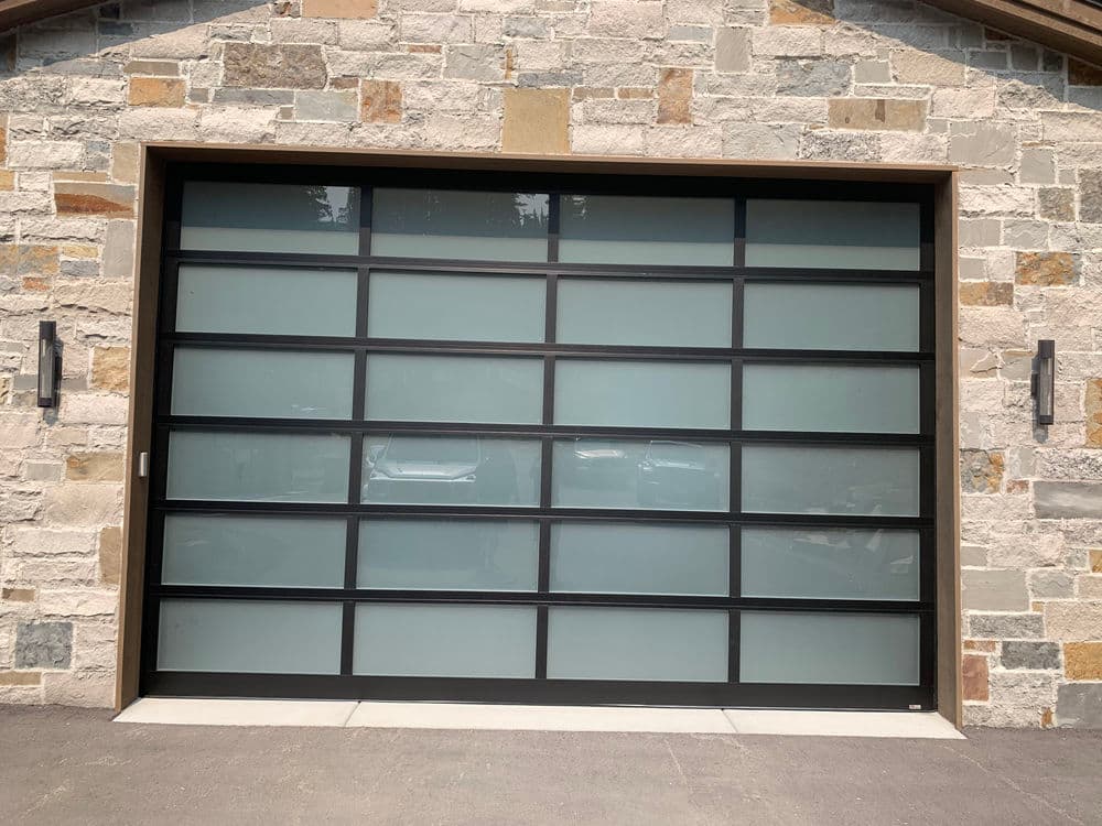 Modern glass garage door with black frame against a stone wall exterior.