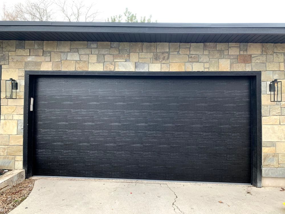 Modern black garage door on a stone wall exterior. Elegant design enhances curb appeal.
