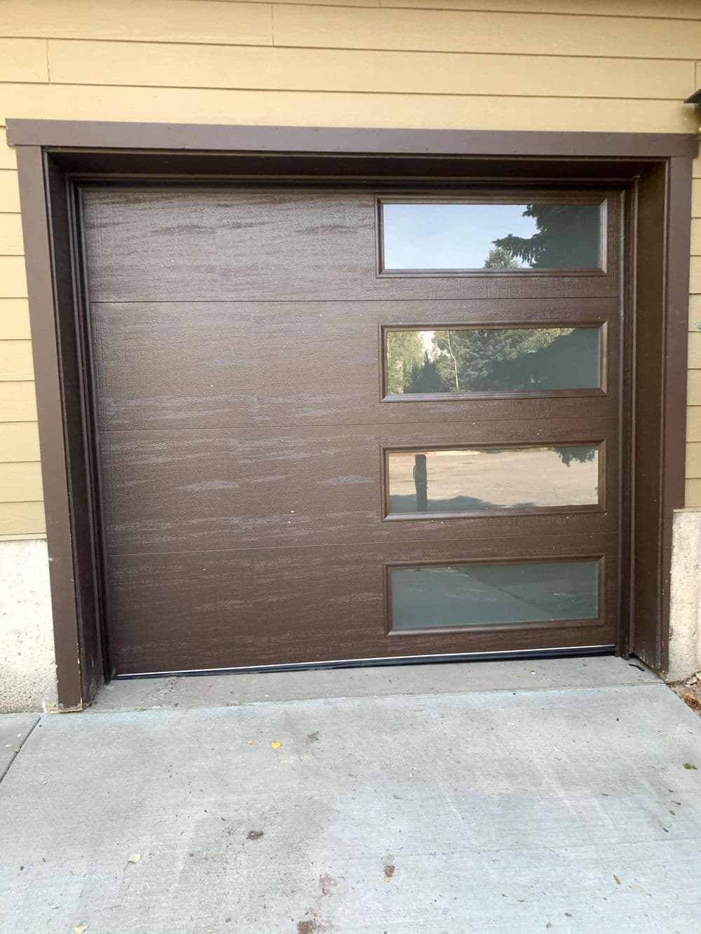 Modern brown garage door with four vertical windows and a textured finish.