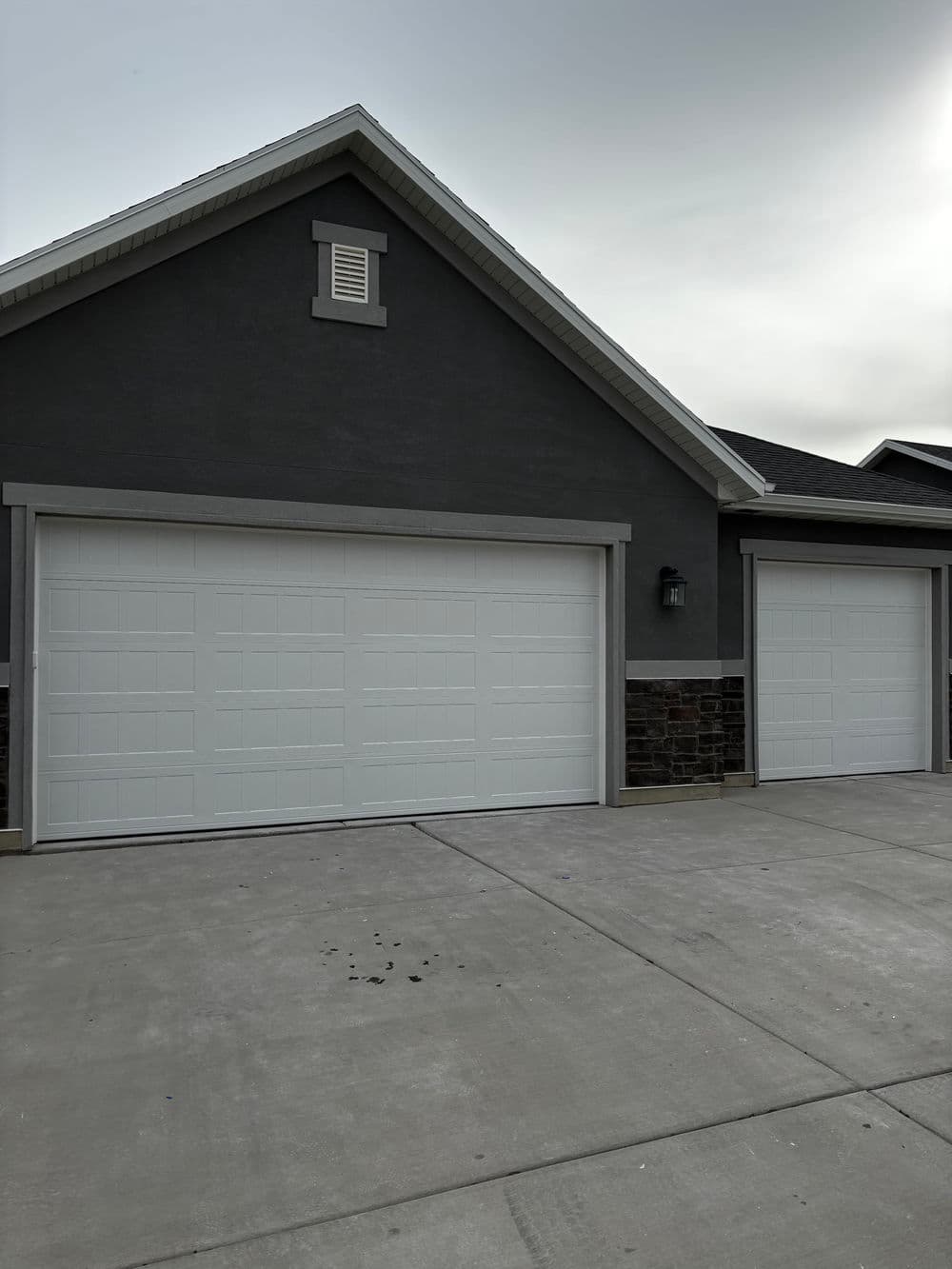 Modern residential garage with two white doors and gray stone accents on the facade.