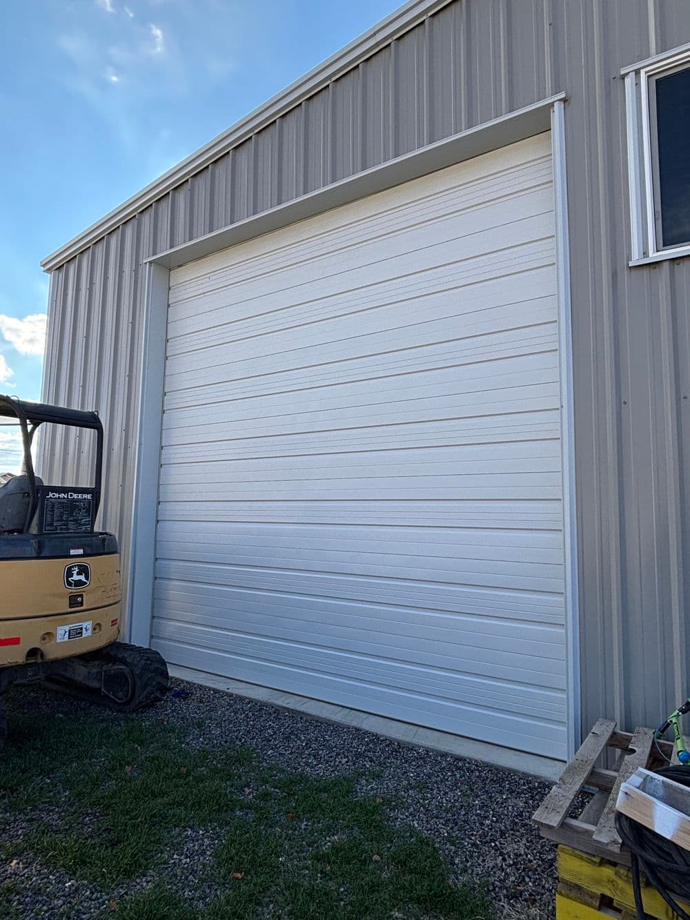 Large white metal garage door on a steel building, with construction equipment nearby.