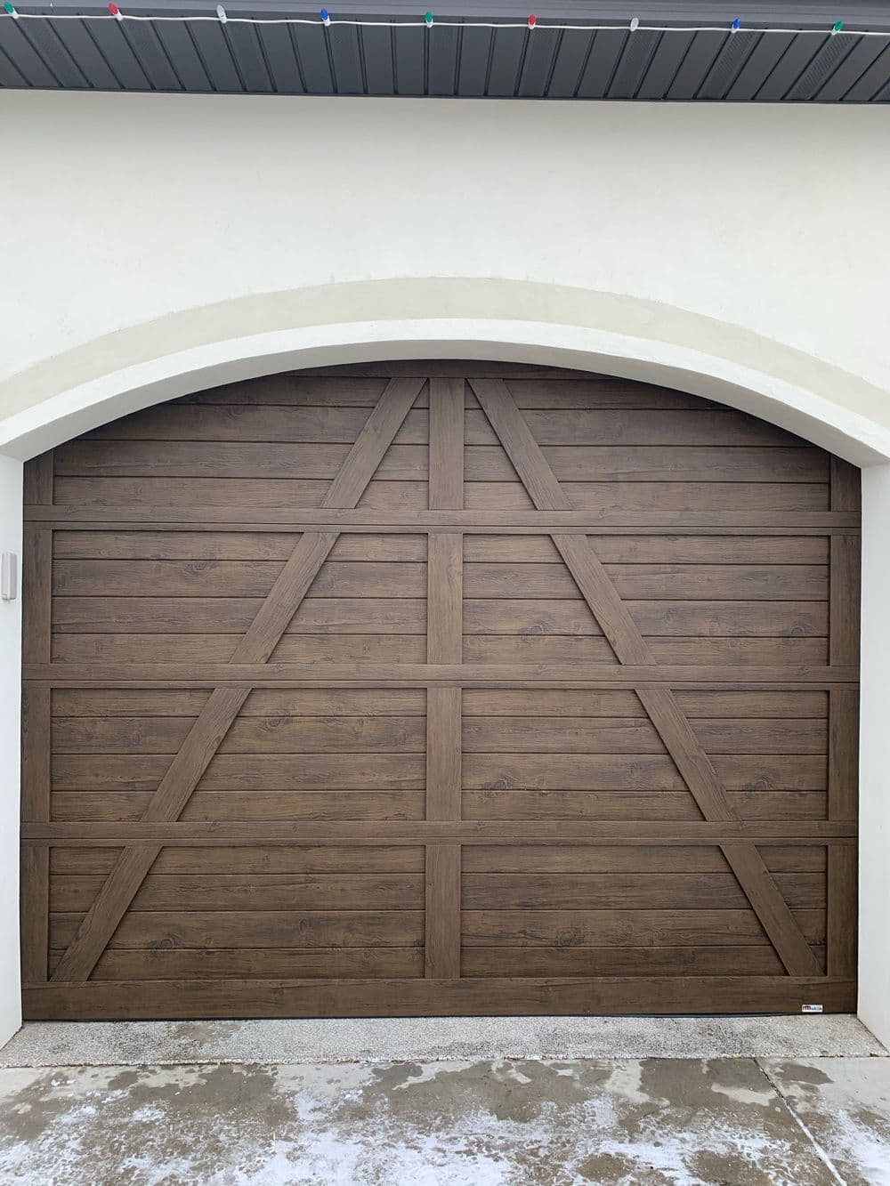 Wooden garage door with a rustic design, featuring diagonal paneling and a curved top.
