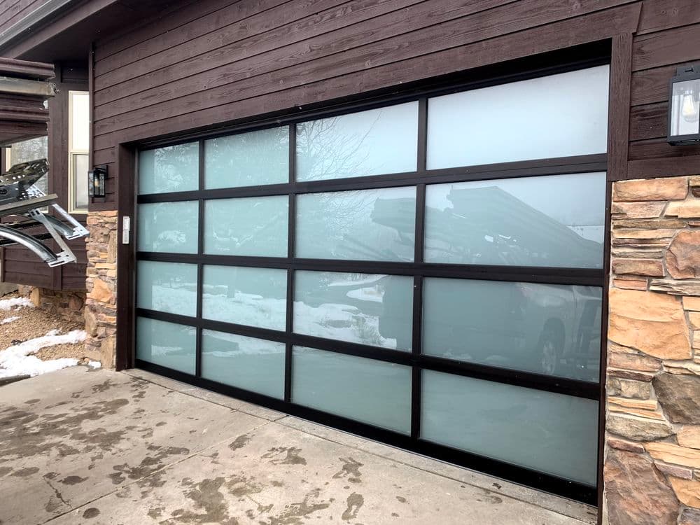 Modern glass garage door with frosted panels on a rustic stone and wood house exterior.