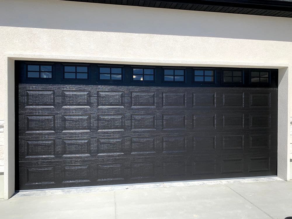 Black garage door with decorative windows and modern design on a residential home.