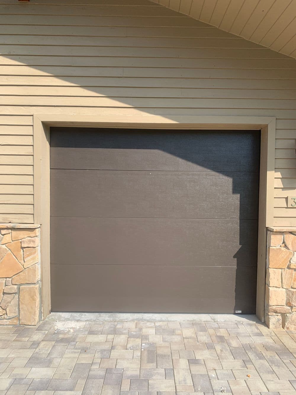 Modern garage door design with stone accents and paved driveway. Ideal for home exterior enhancements.