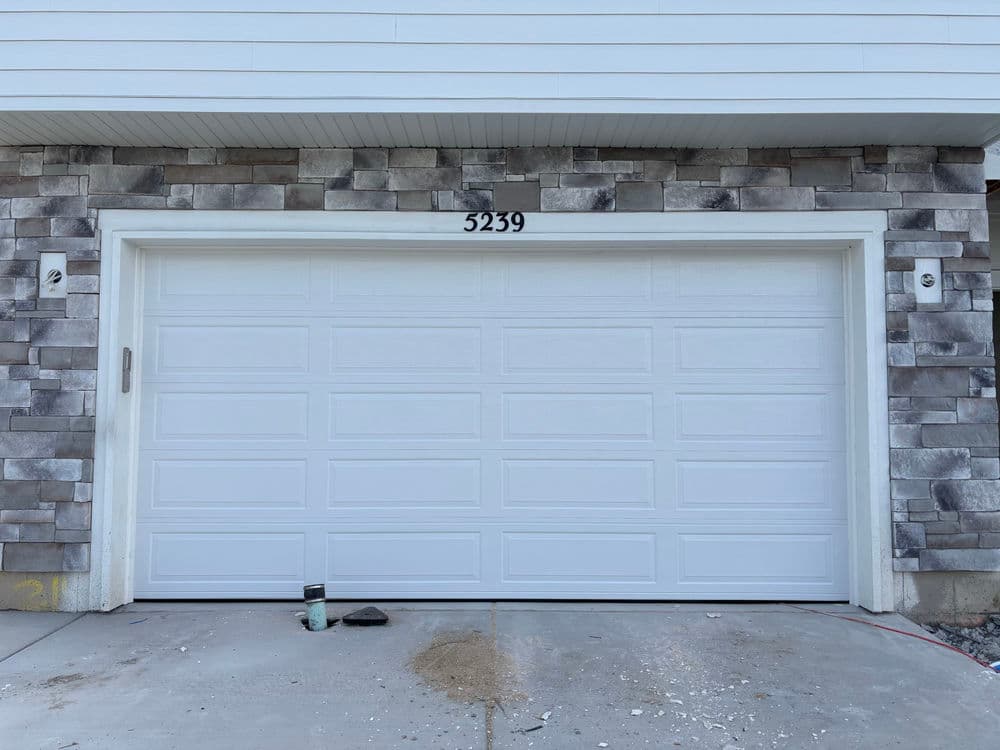 White garage door with gray stone exterior and house number 5239. Tools nearby on concrete.
