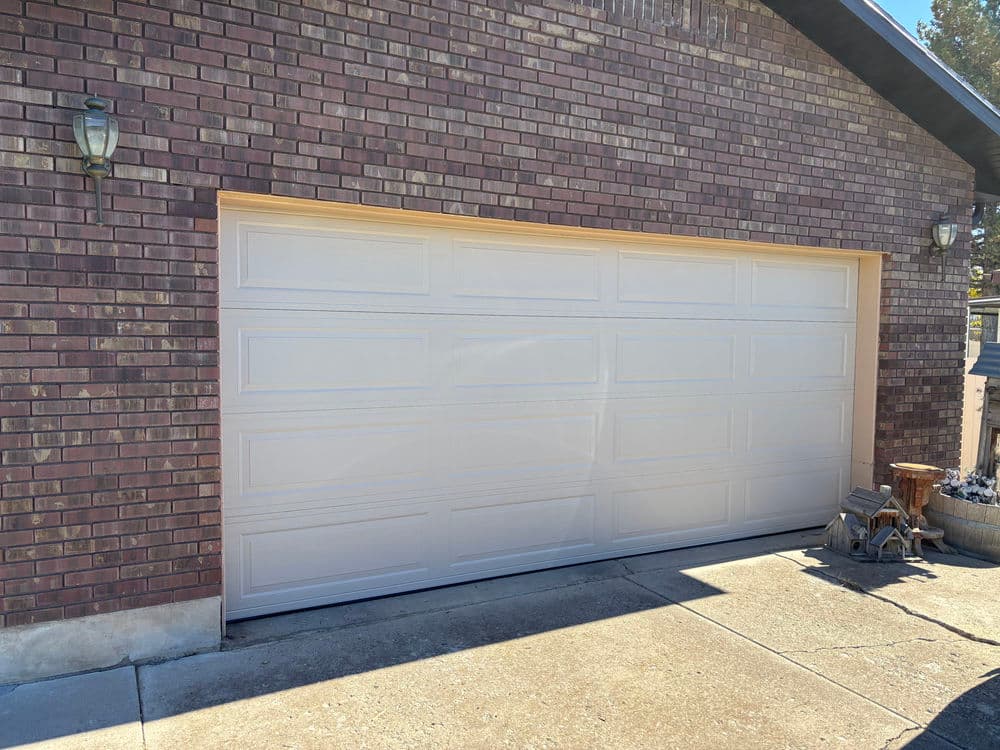 White garage door on a brick house exterior with a concrete driveway and outdoor decor.
