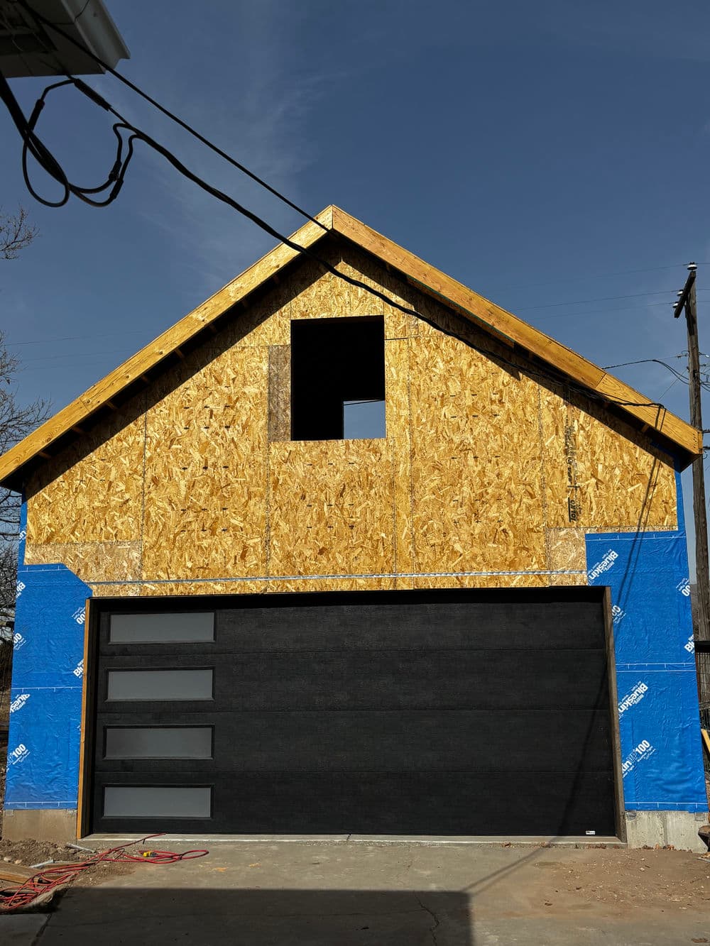 Newly constructed garage with wooden frame, blue sheathing, and modern black garage door.