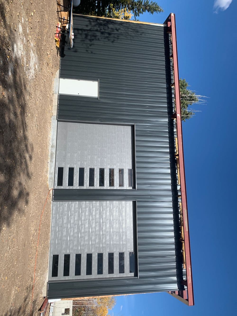 Modern metal building with a large garage door against a clear blue sky.