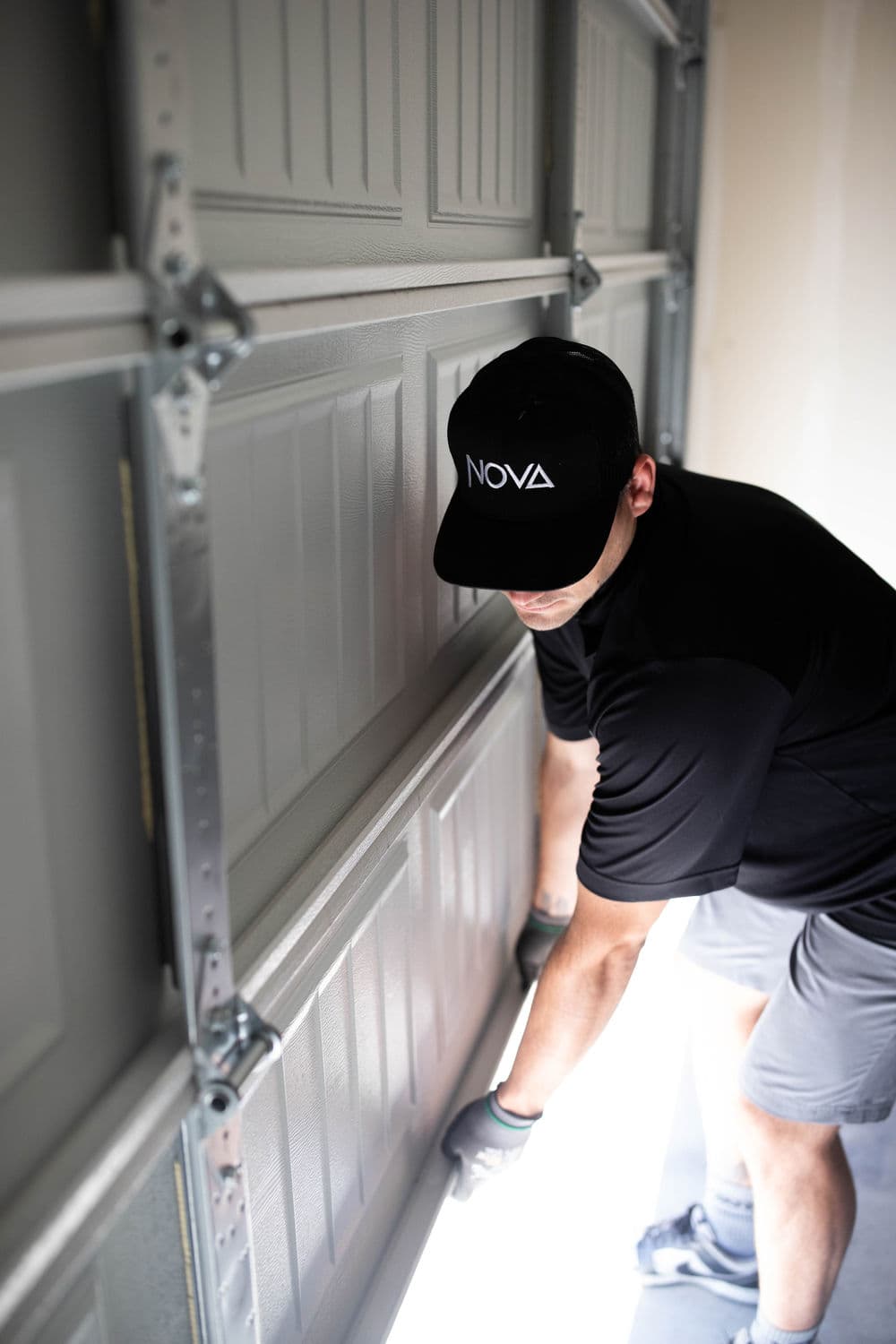 Man in a black hat and shirt installing a garage door, emphasizing home improvement.