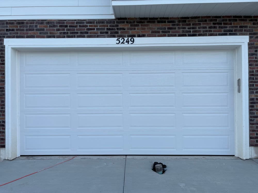 White garage door with panel detailing, house number 5249, set against a brick wall.