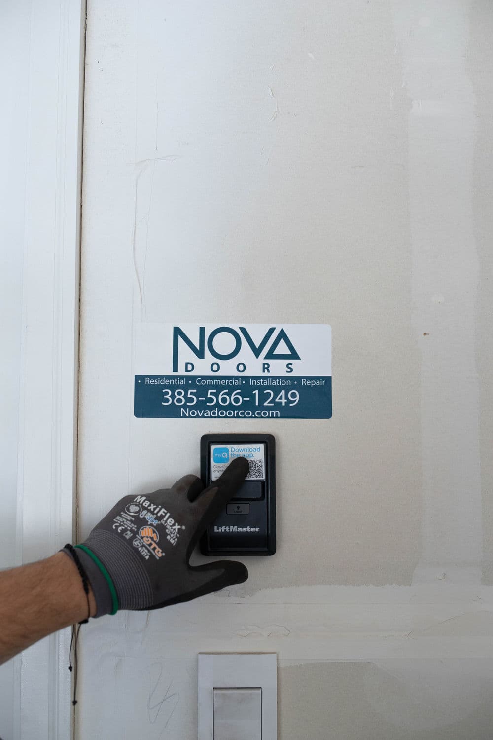 Hand reaching for a LiftMaster door control, featuring NOVA Doors sign for installation and repair.