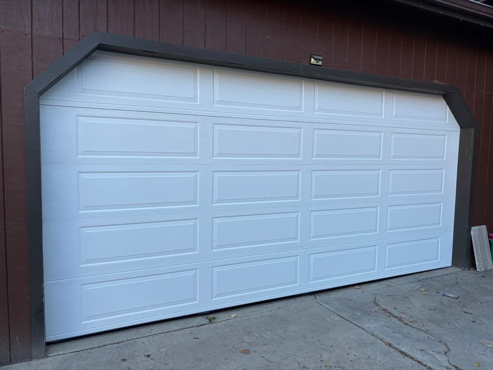 White residential garage door with a modern design, set against a brown wall.
