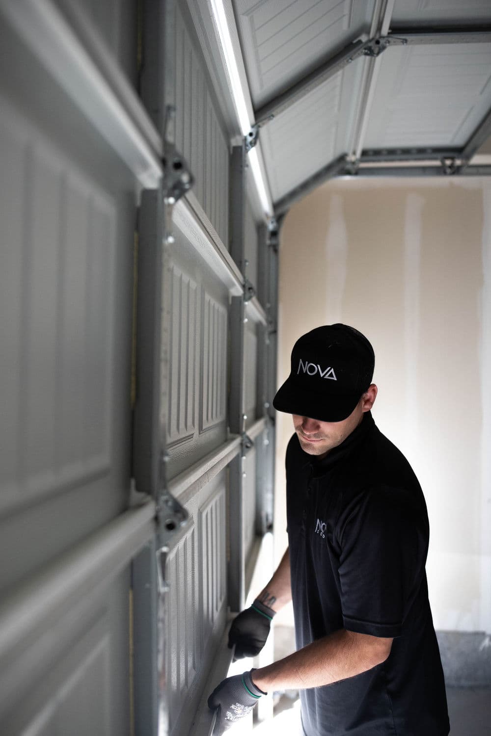 Garage door installation by a technician wearing a black NOVA cap and shirt.