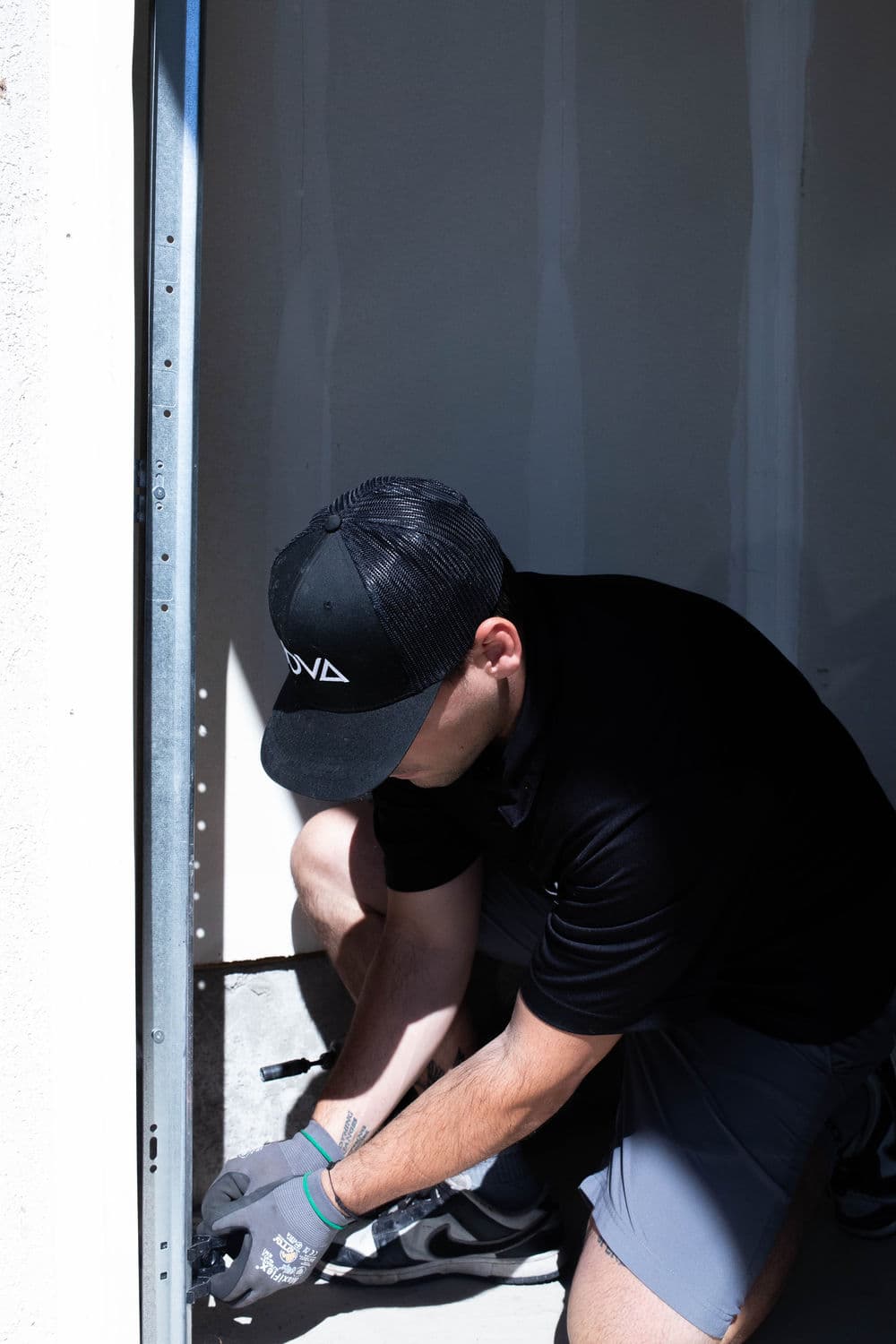 Worker installing a metal frame in a construction site, wearing a black cap and gloves.