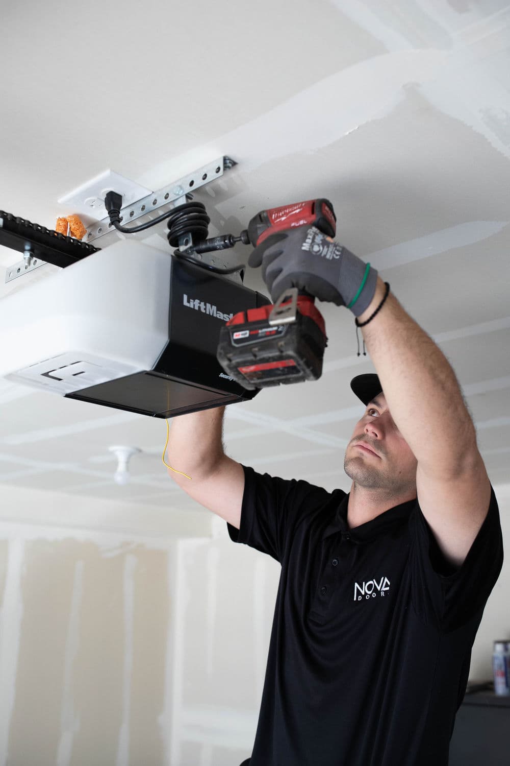 Technician installing LiftMax garage door opener with power tools in residential garage.
