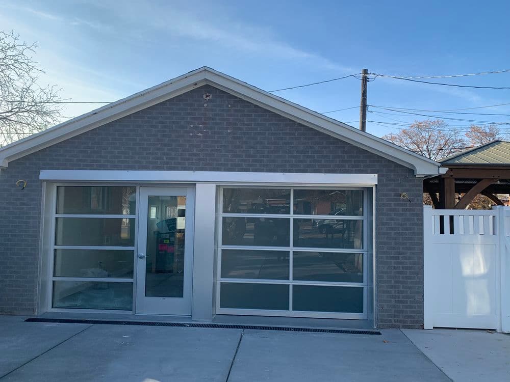 Modern gray brick building with large glass doors and a white fence. Clear blue sky above.