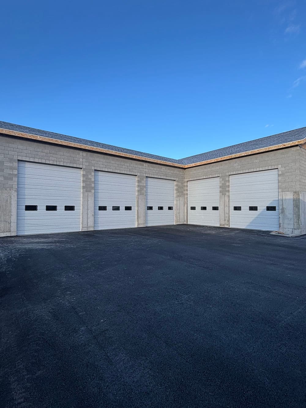 Newly constructed storage facility with multiple garage doors and clear blue sky.