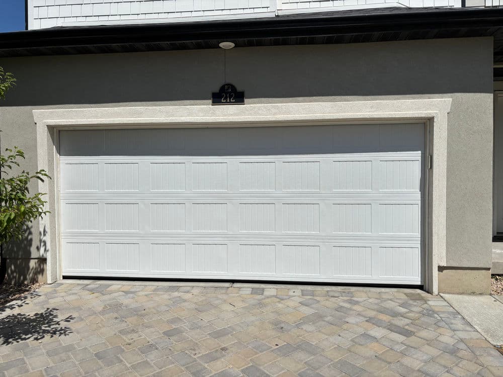 White garage door with panel design on a modern home, viewed from a stone driveway.