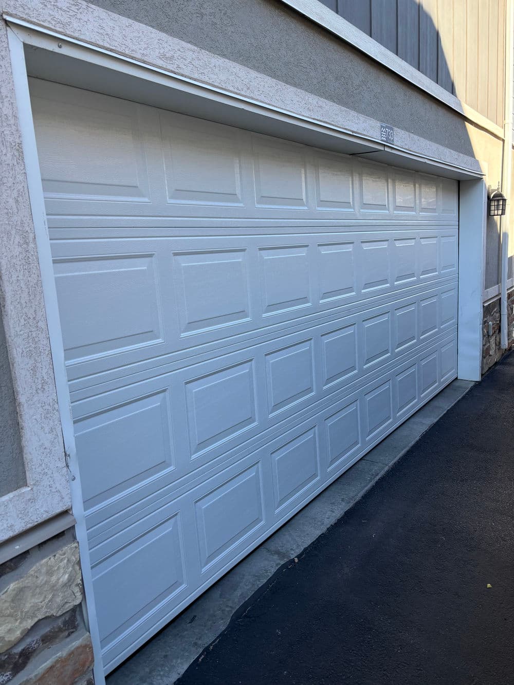 White garage door with a textured design, set against a stone and concrete exterior.