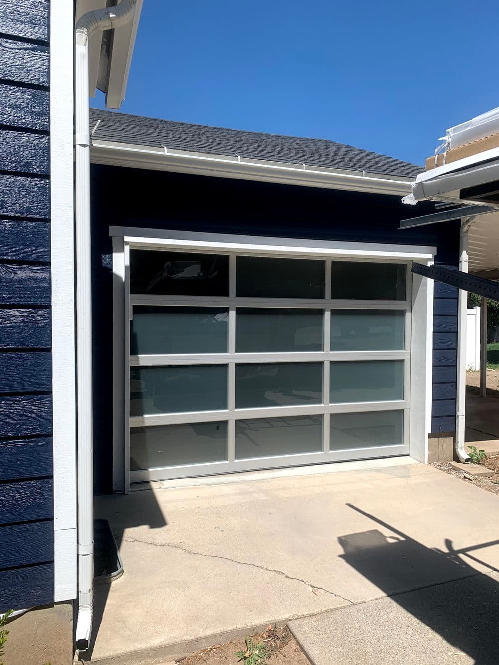 Modern garage with large windows, blue exterior, and concrete driveway under clear sky.