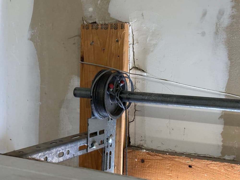 Garage door spring mechanism mounted on wall, showing tension cables and pulley system.