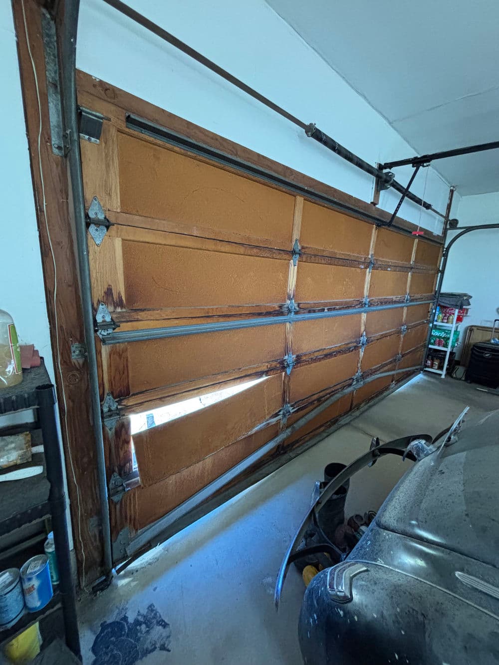 Wooden garage door with metal tracks, partially open, revealing car beyond.