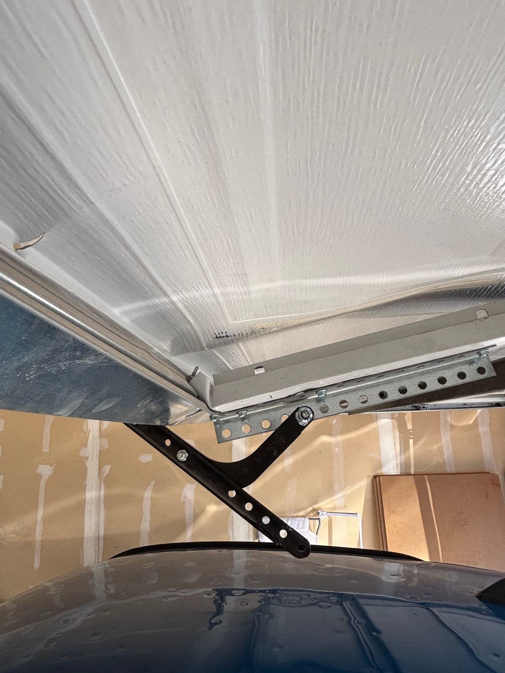 Garage door hinge mechanism with partially opened panel and floor details.