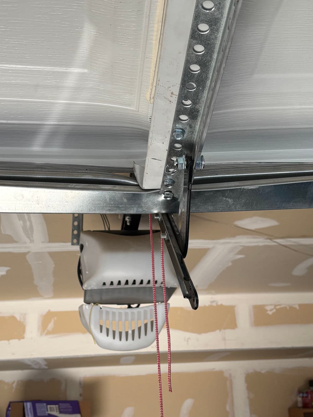 Garage door opener mechanism with metal tracks and safety features, installed in a garage.