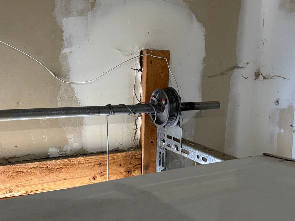 Barbell resting on a metal rack in a garage gym with exposed wooden beams and walls.
