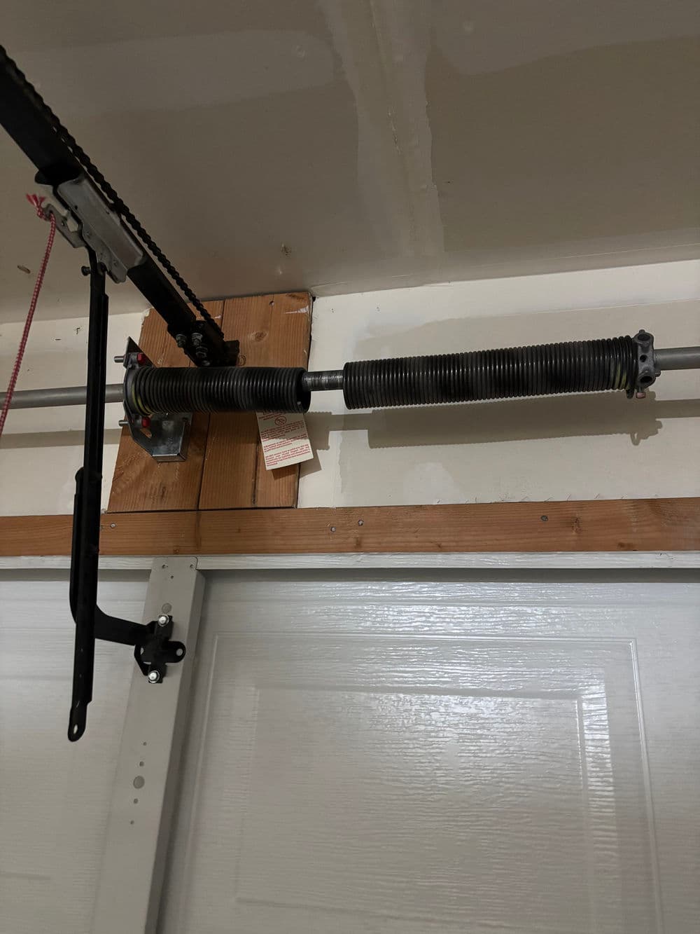 Garage door torsion spring mechanism installed on the wall with safety warning tag.