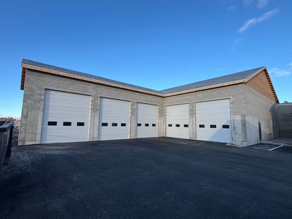 Newly built storage facility with multiple garage doors and a clear blue sky.