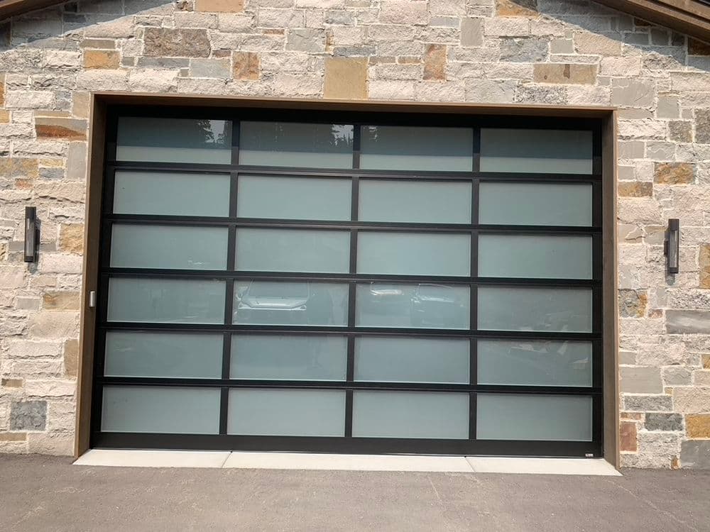 Modern black framed glass garage door against a textured stone wall, showcasing contemporary design.