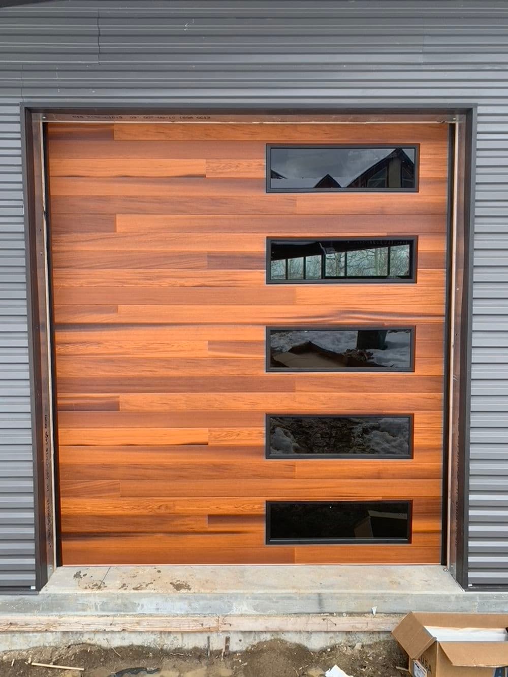 Wooden garage door with four rectangular glass windows and horizontal wood paneling.