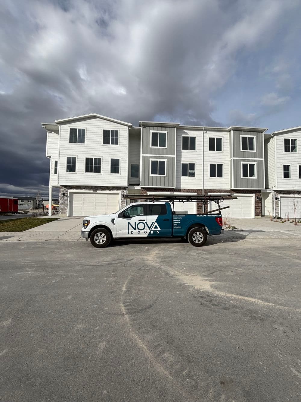 Nova Doors vehicle parked in front of a modern townhome complex under cloudy skies.