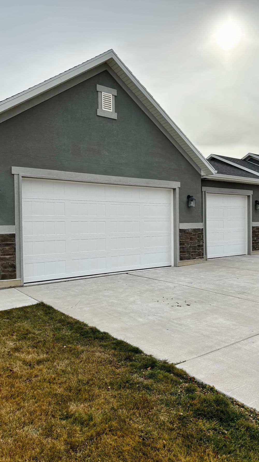 Two modern garage doors on a gray house exterior with a concrete driveway and grass.