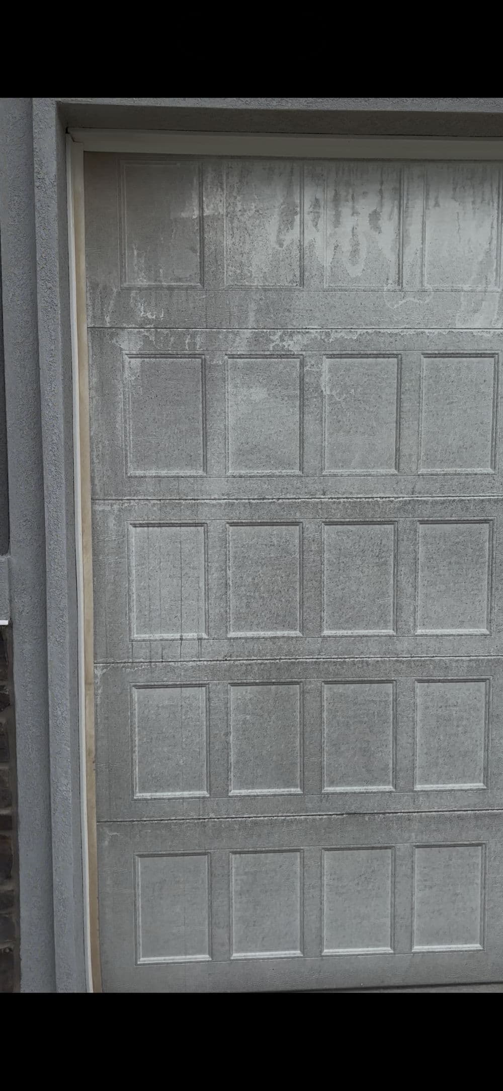 Gray garage door with textured panels and slight wear, set against a stone wall.