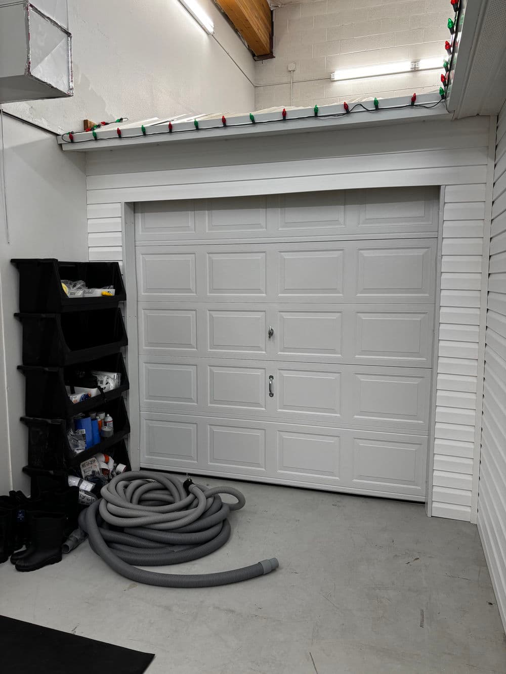White garage door in a clean garage with storage bins and a coiled hose.