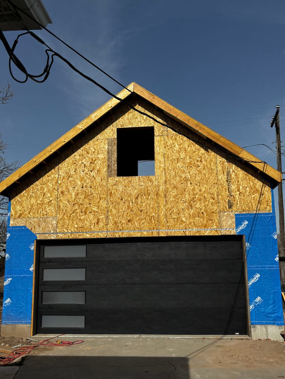 Newly constructed garage with wooden frame, open window, and blue insulation sheathing.