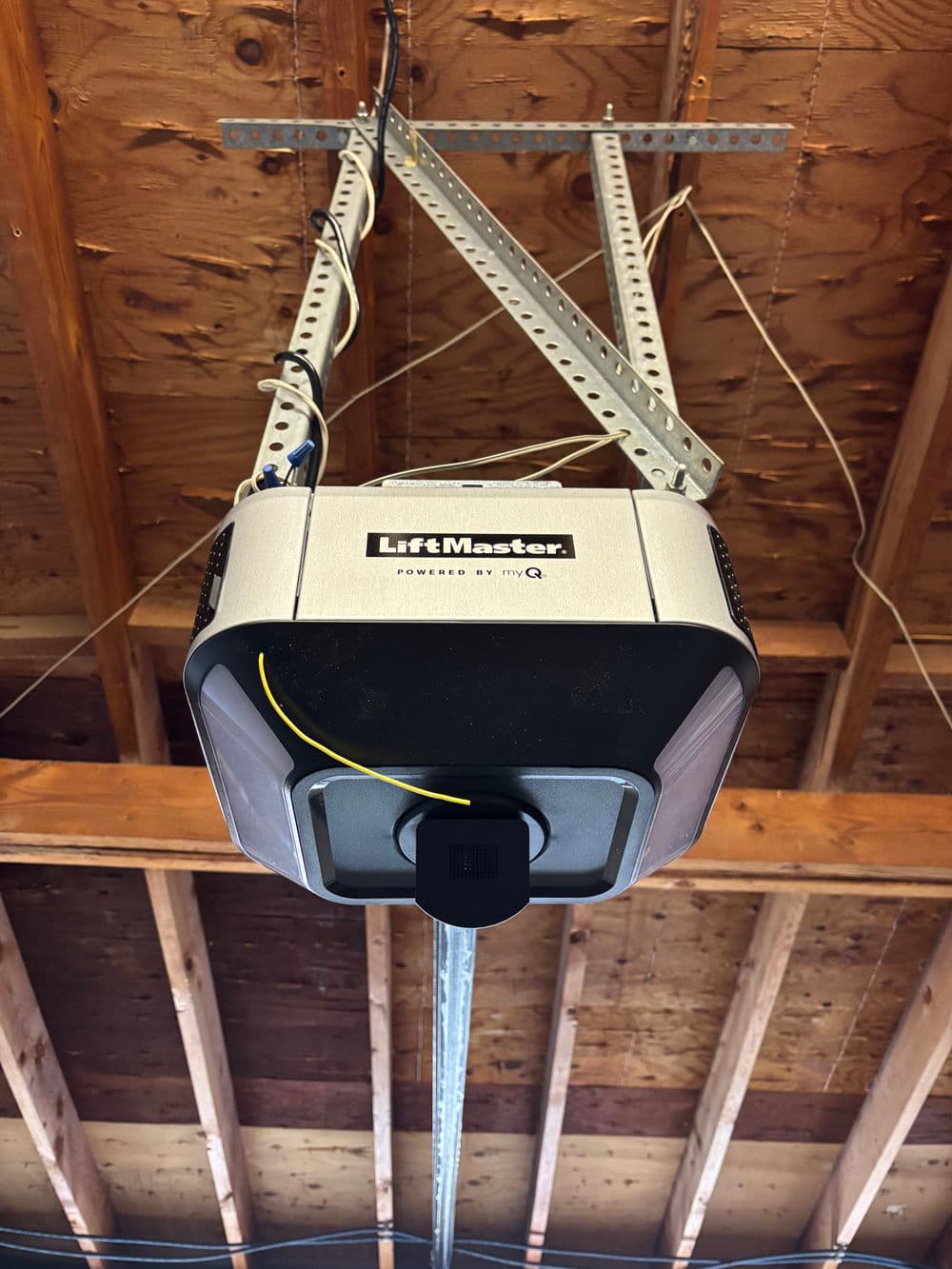 LiftMaster garage door opener mounted overhead in wooden ceiling with visible electrical wiring.