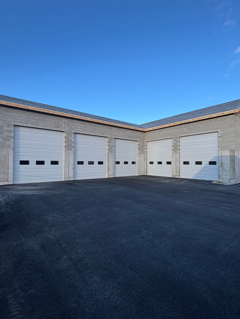 New industrial garage with four white overhead doors and a clear blue sky.