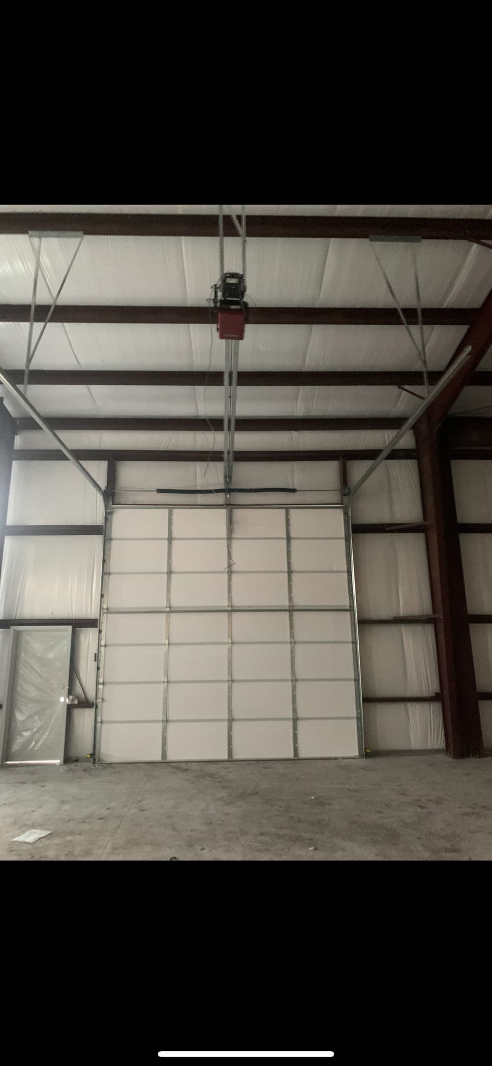 Interior of a large warehouse showing a sectional garage door and industrial space.