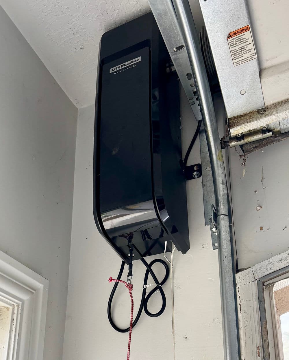 Black garage door opener mounted on a wall with visible wiring and safety features.