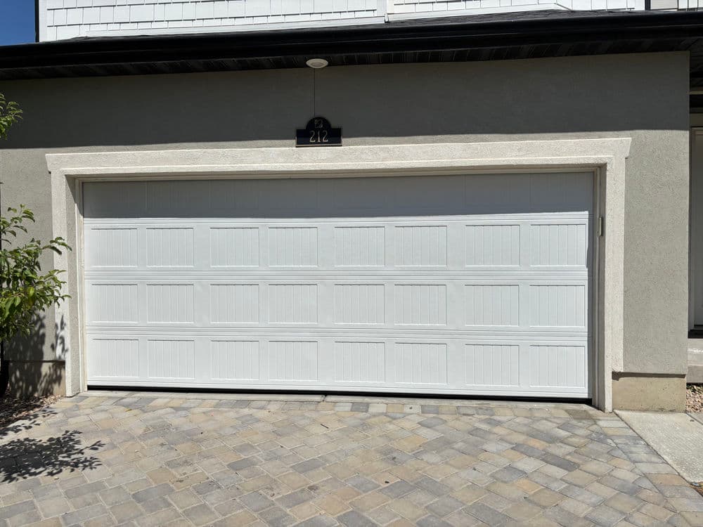White garage door with horizontal panels and cobblestone driveway in front of a house.