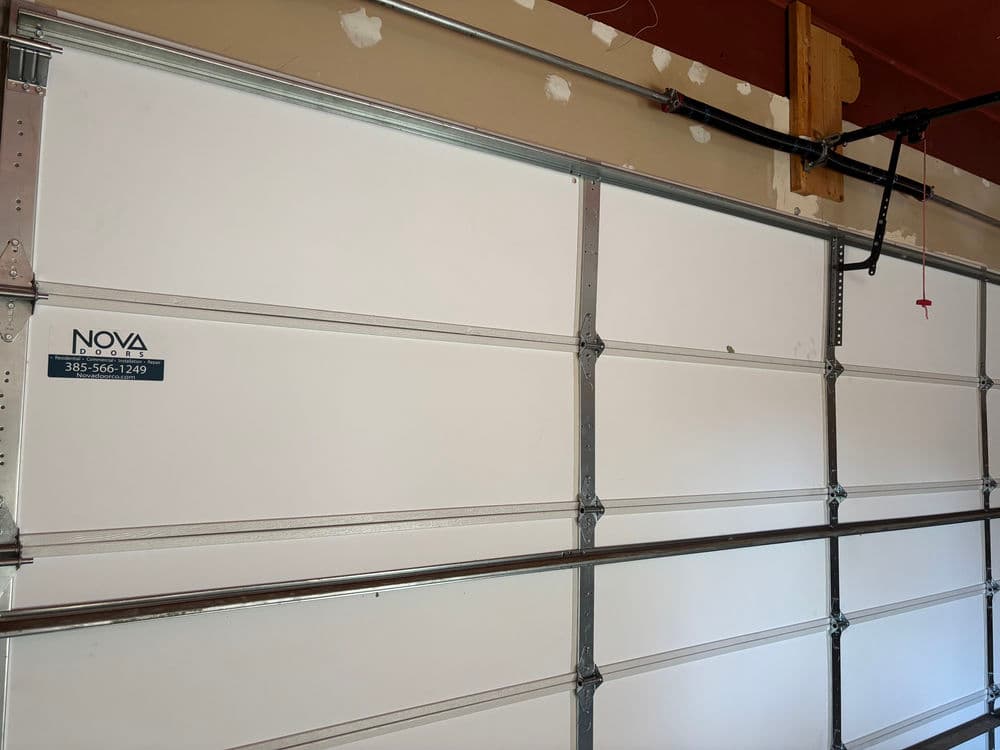 White garage door with metal tracks, featuring a Nova service sticker and phone number.