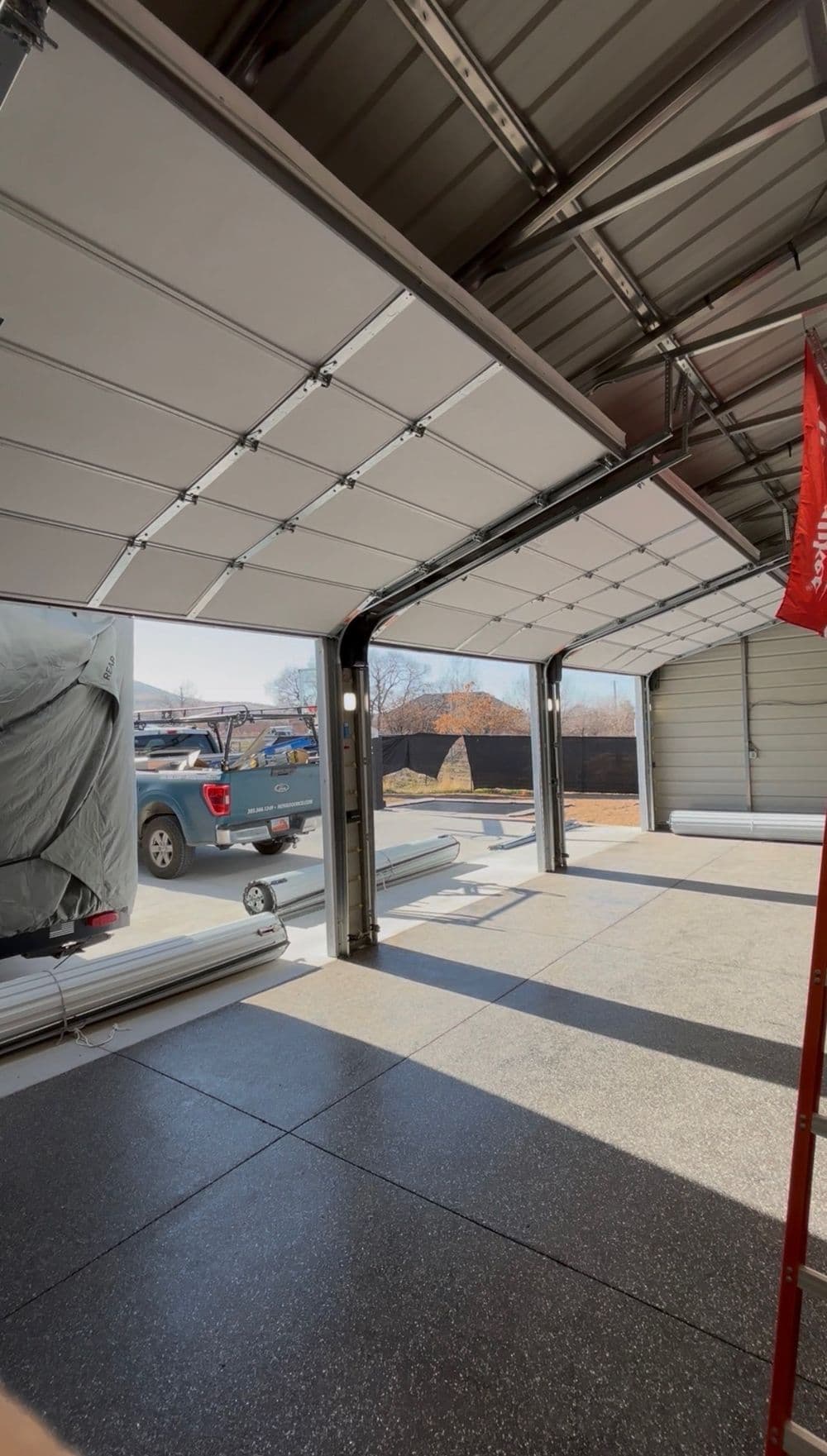 Interior of a modern garage with open doors, concrete floor, and trucks outside.