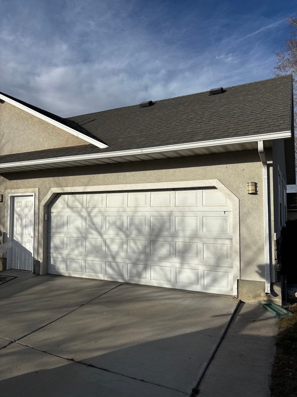 Two-car garage with white door, gray exterior, and clear sky in the background.